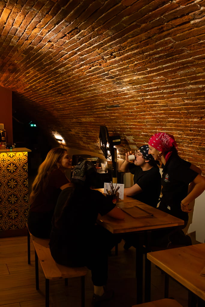 Clients du bar espagnol BOCA à Toulouse, attablés en cave pour déguster des tapas et des boissons ibériques, dans une ambiance festive et authentique, entre murs en briques et lumière chaleureuse.